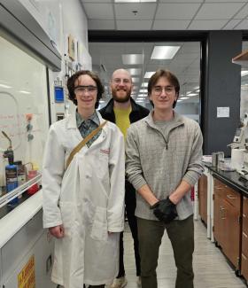 High school student Copper Callahan, science teacher Robert Pulliam, and UGA Chemistry graduate student Skyler Hollers stand in an organic chemistry lab with fume hood and lab bench in the background