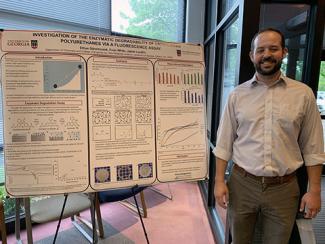 Photo of speaker Ethan Stinchcomb posed next to a poster presentation of the subject