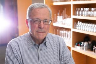 Portrait of Dr. John Richard, guest speaker, with a background of lab equipment on shelves
