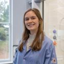 image depicts causasian woman with long brown hair, standing in front of a laboratory fume hood