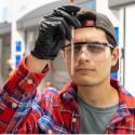 Image depicts young man in a lab, peering at the contents of a tube