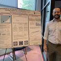 Photo of speaker Ethan Stinchcomb posed next to a poster presentation of the subject