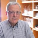 Portrait of Dr. John Richard, guest speaker, with a background of lab equipment on shelves