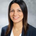 Headshot of speaker; female with dark hair and eyes, wearing white shirt and navy blue jacket